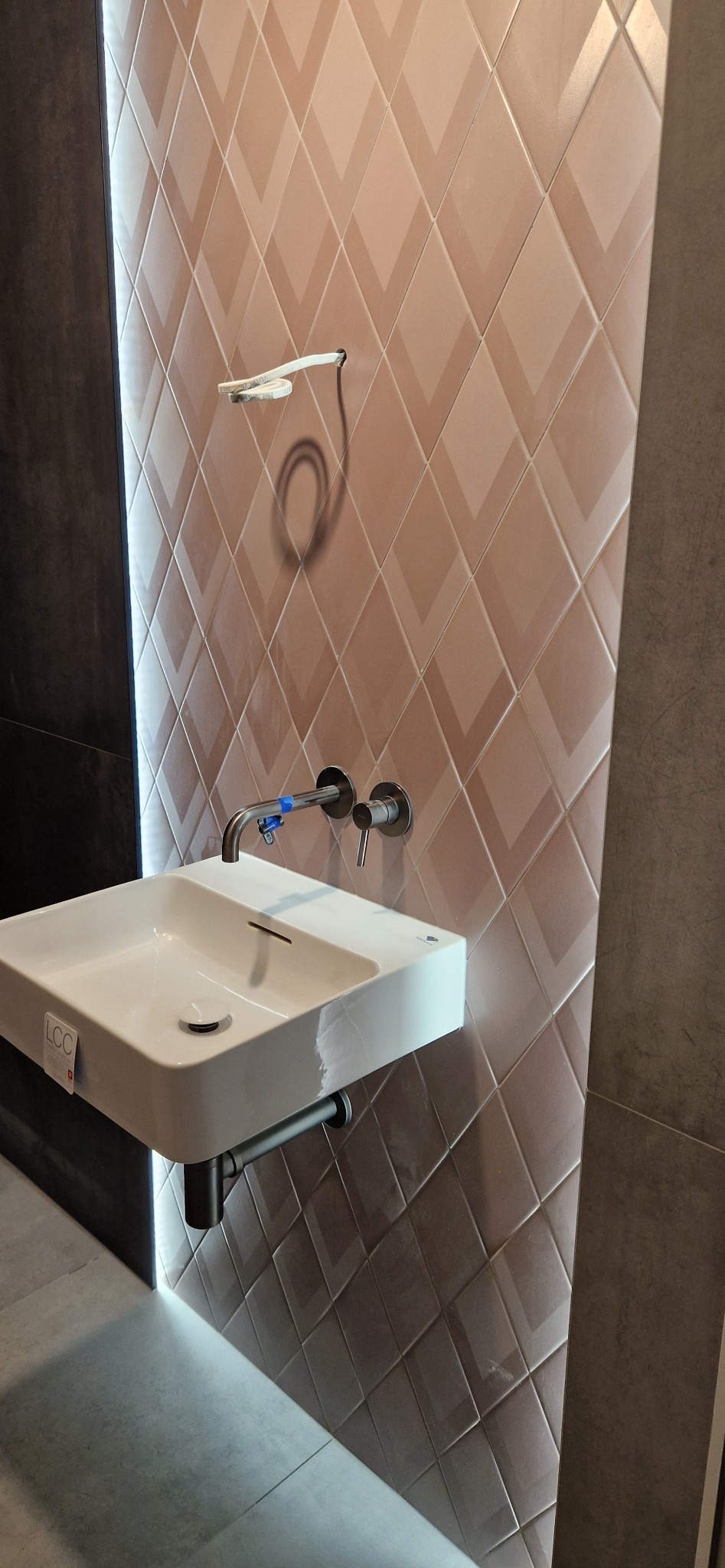 Nowoczesna, biała umywalka z chromowaną baterią zamontowana na tle ściany wyłożonej kafelkami w romby w odcieniach beżu i brązu, widok z bliska, Łambinowice.