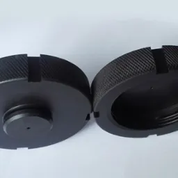 Dwie czarne, okrągłe, metalowe nakrętki z gwintem wewnętrznym i zewnętrznym, leżące obok siebie na białym tle, z widocznymi detalami obróbki skrawaniem.