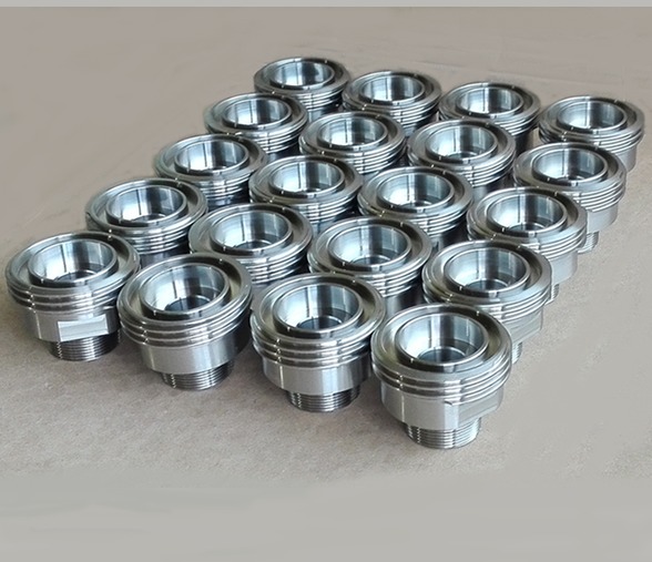 Partia precyzyjnie wykonanych, metalowych detali z gwintem, ułożonych w rzędach na neutralnym tle, z widocznymi śladami obróbki.