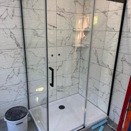 Andrzej Dobrovolskyi - Nowoczesna kabina prysznicowa z czarnymi profilami i marmurowymi płytkami na ścianach. Widoczne narzędzia i wiadro, sugerujące świeży montaż.