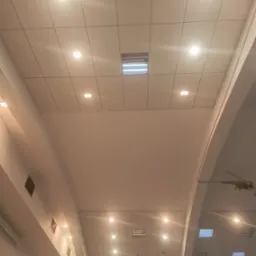 Sufit z płyt kartonowo-gipsowych z wbudowanym oświetleniem punktowym i kratkami wentylacyjnymi, widoczny łuk architektoniczny i instalacja oświetleniowa.