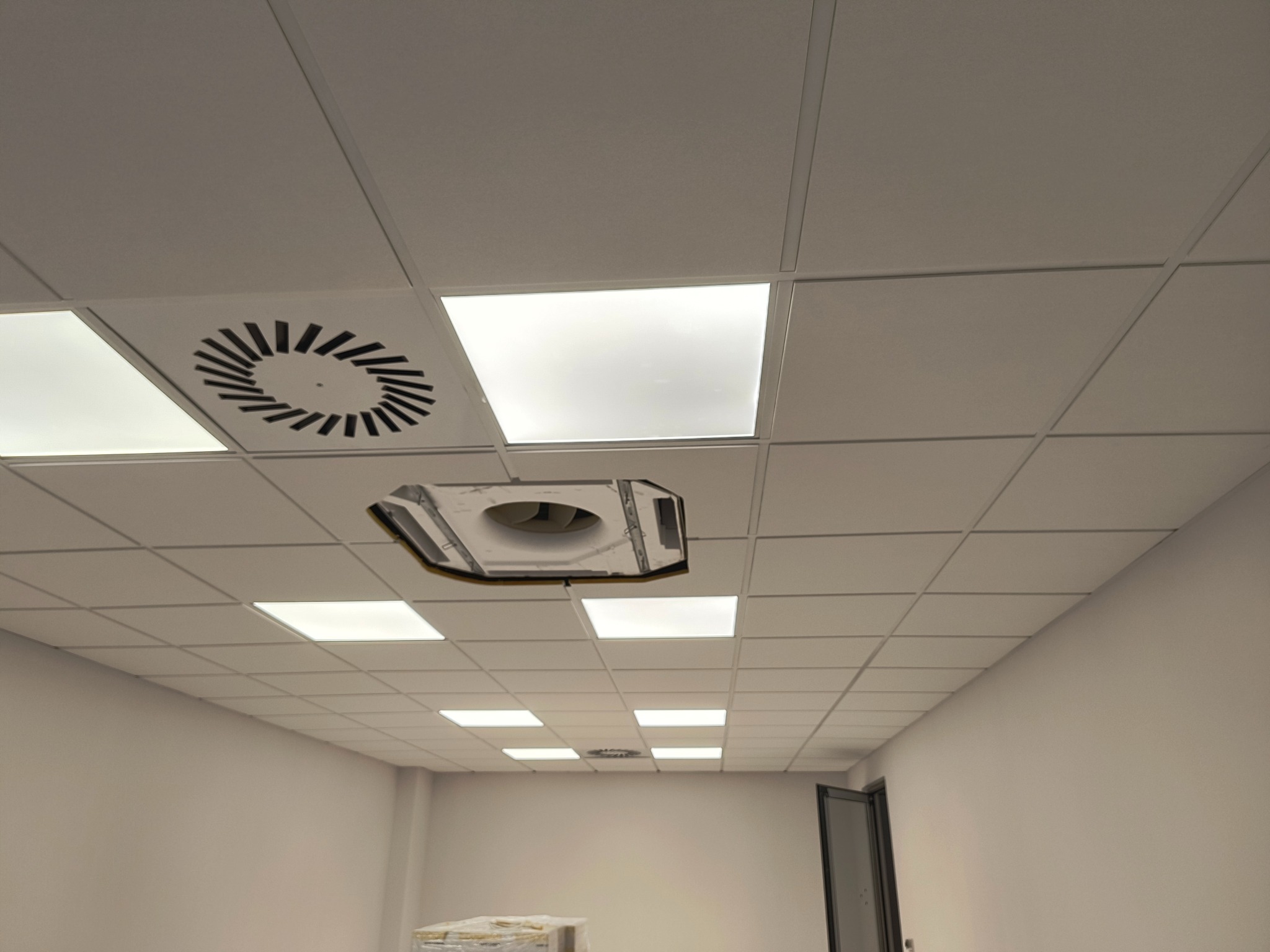 Kasetonowy sufit podwieszany z wbudowanym oświetleniem LED i kratką wentylacyjną, widoczny fragment instalacji klimatyzacji w przestrzeni biurowej.
