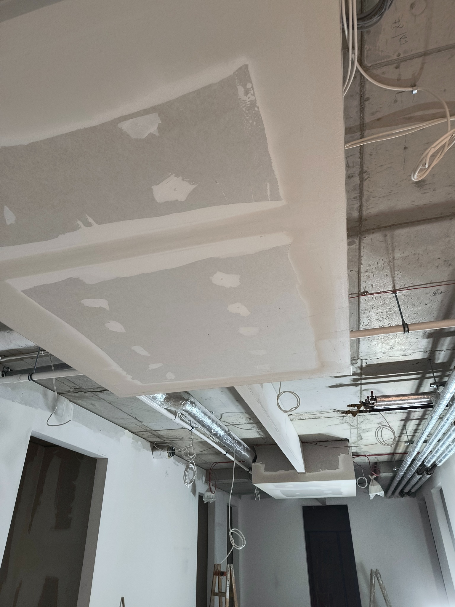 Montaż płyty karton gips na suficie w trakcie prac wykończeniowych, widoczne instalacje, rury wentylacyjne i fragmenty ścian