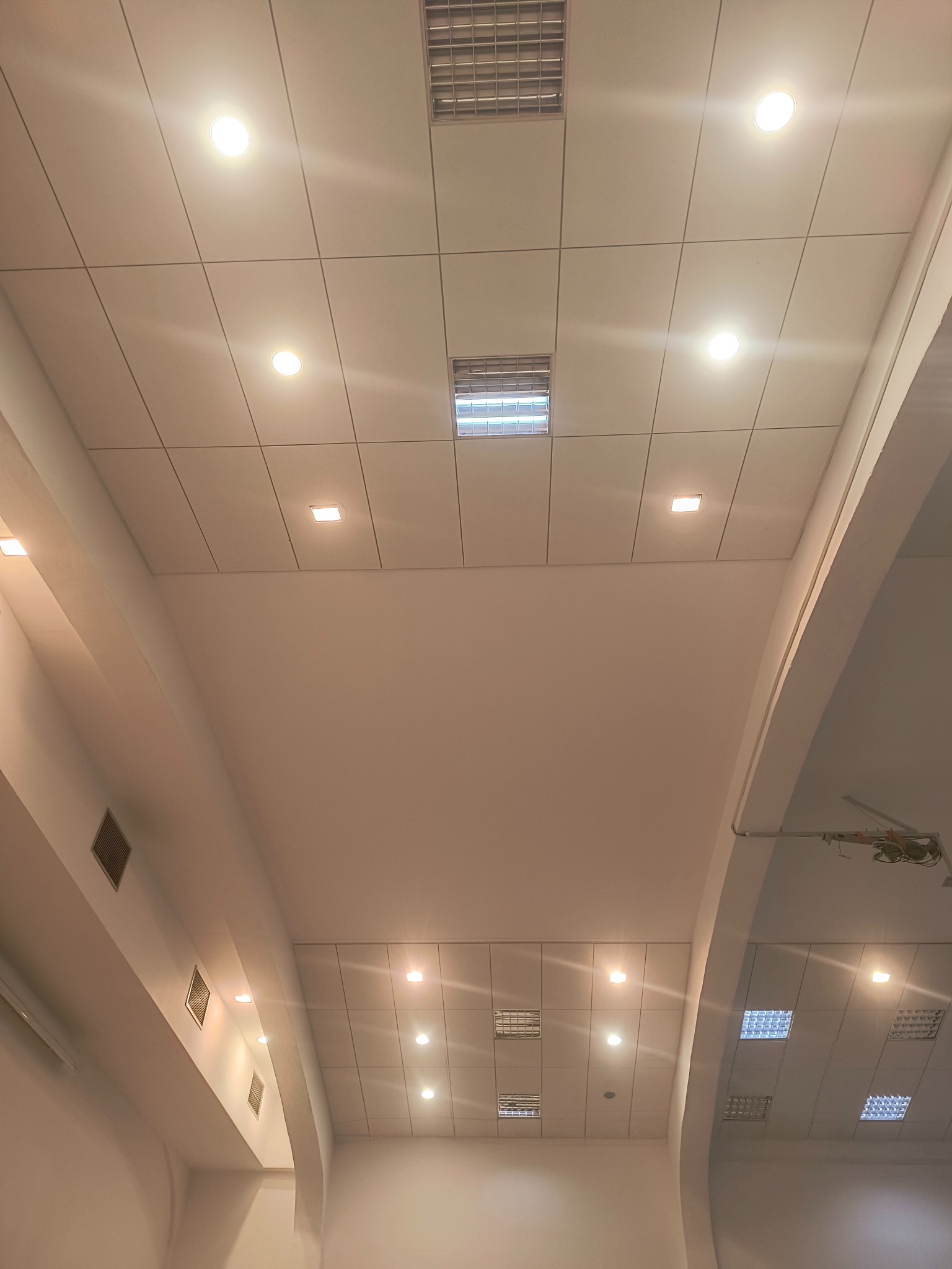 Sufit z płyt kartonowo-gipsowych z wbudowanym oświetleniem punktowym i kratkami wentylacyjnymi, widoczny łuk architektoniczny i instalacja oświetleniowa.
