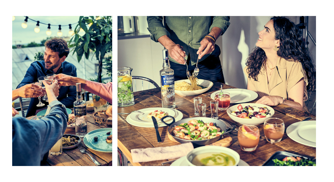 Uroczysty obiad na świeżym powietrzu: grupa osób wznosi toast kieliszkami, na stole butelka wódki Wyborowa, przystawki i drinki. Wnętrze kuchni z osobą nakładającą spaghetti, różne dania i napoje...