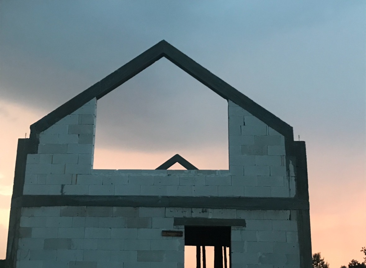 Surowy stan budynku z betonu komórkowego z widocznym zarysem dachu na tle zachodzącego słońca.