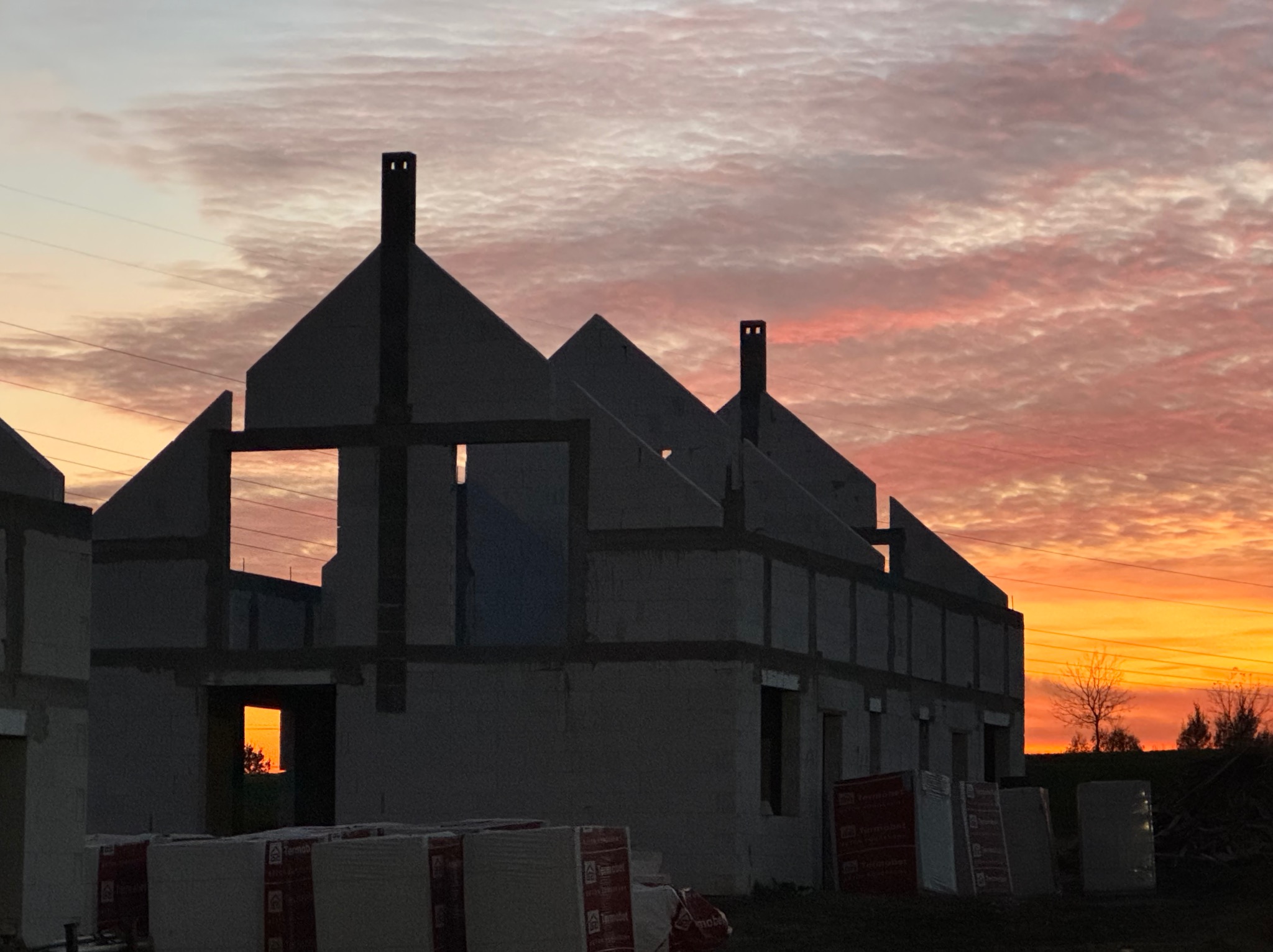 Surowy stan budynku z betonu komórkowego, widok na zachód słońca przez otwory okienne i drzwiowe, palety bloczków budowlanych na pierwszym planie.