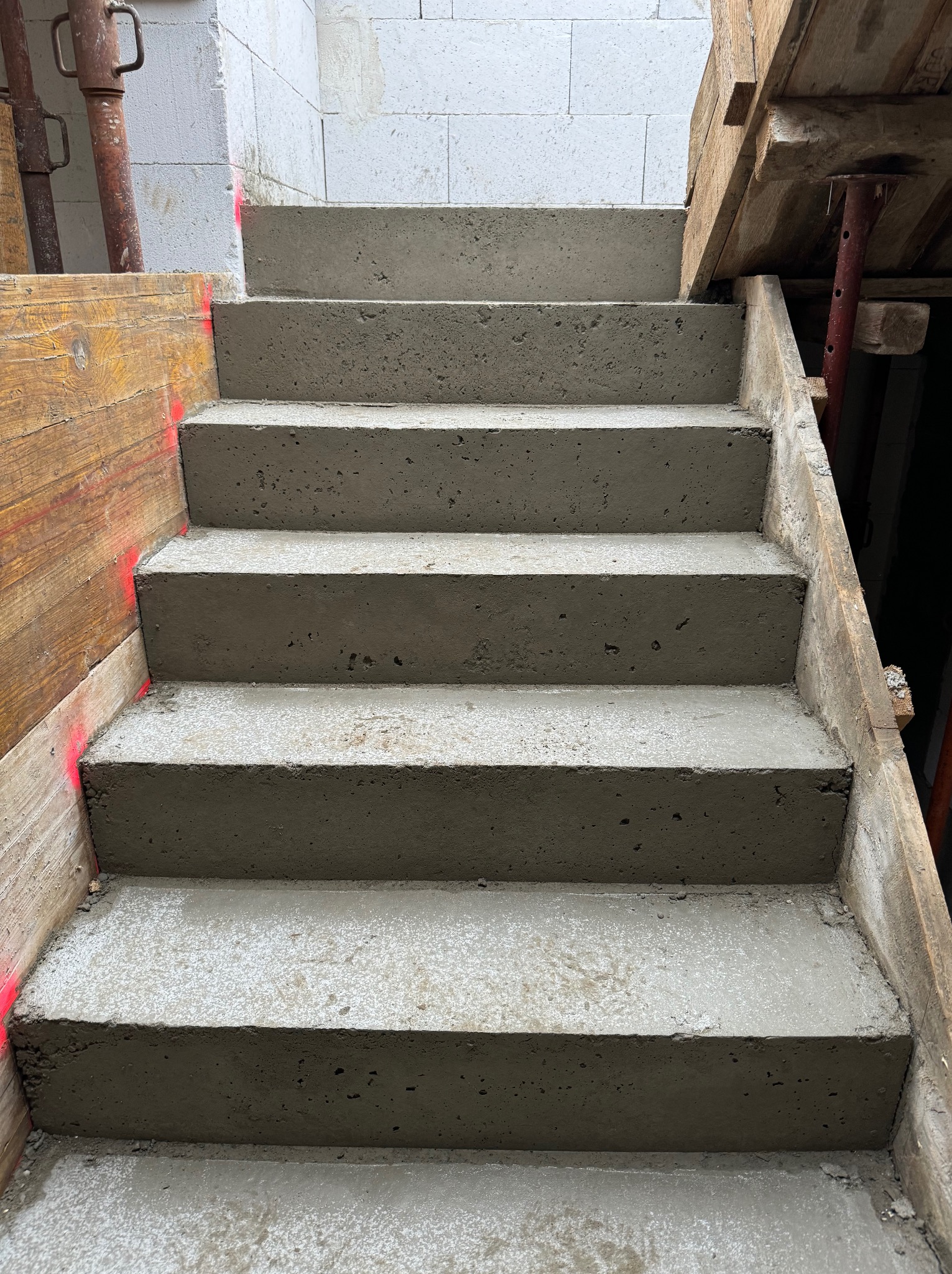 Surowe betonowe schody wewnętrzne w trakcie budowy, z widocznym szalunkiem z desek i bloczkami z betonu komórkowego w tle.