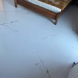 Błyszcząca, biała posadzka z szarymi żyłkami imitującymi marmur w sypialni z drewnianym łóżkiem i grzejnikiem na ścianie.