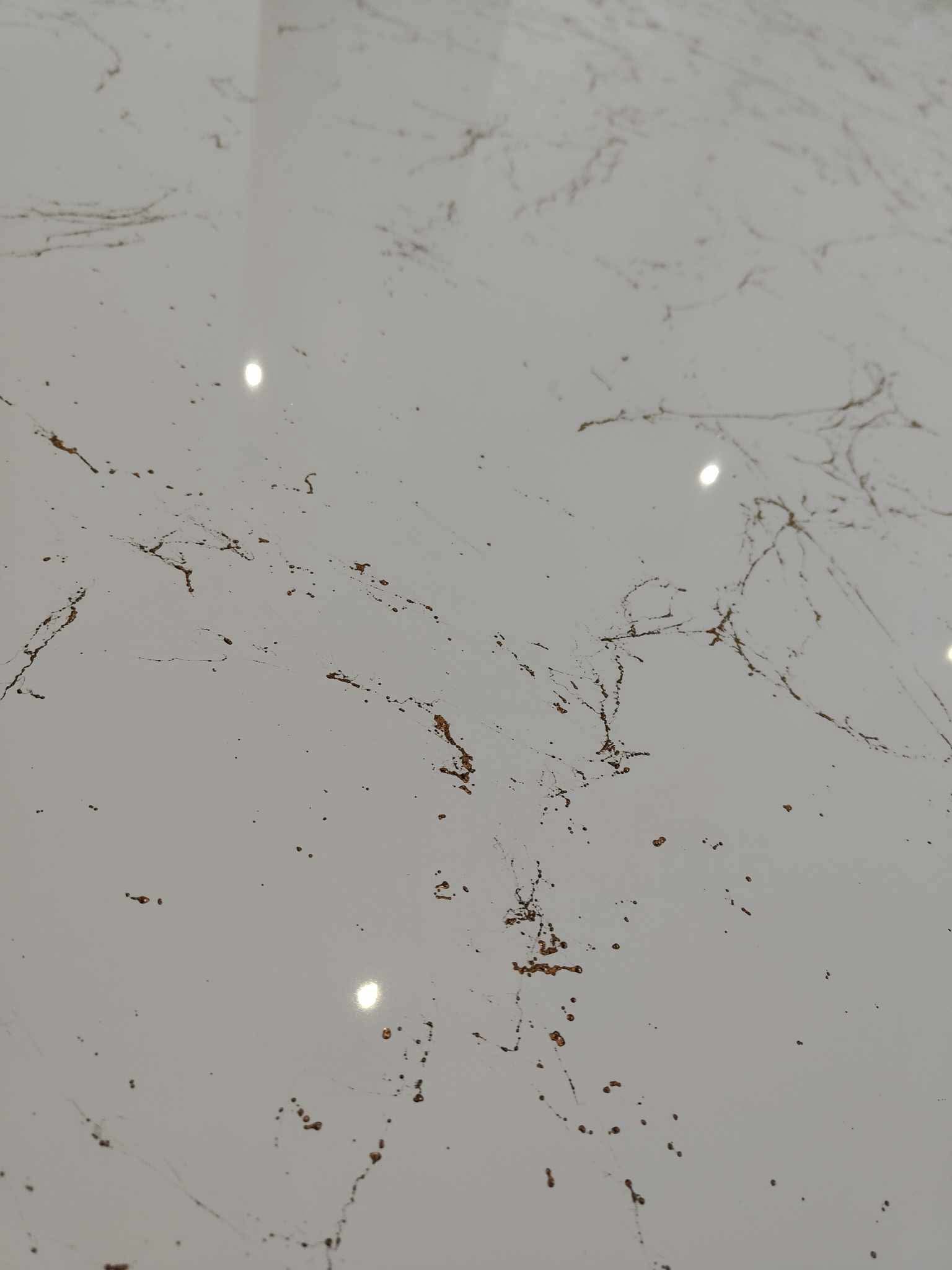 Jasnoszara posadzka z delikatnym, nieregularnym wzorem w odcieniach brązu i złota, połyskująca pod wpływem światła.