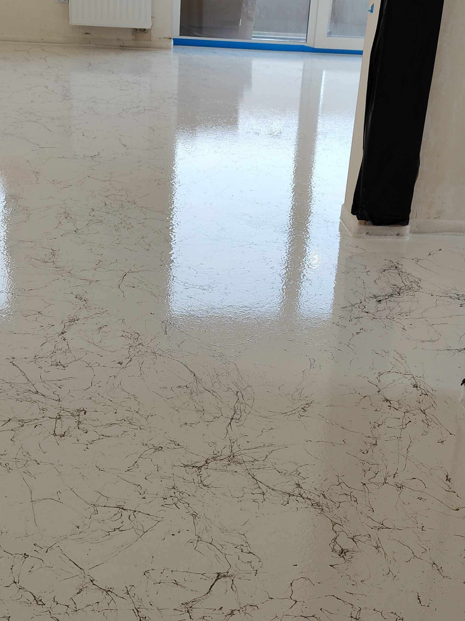 Błyszcząca, biała posadzka z delikatnym, brązowym wzorem żyłkowania, odbijająca światło okien, w pomieszczeniu w Tomaszowie Mazowieckim.