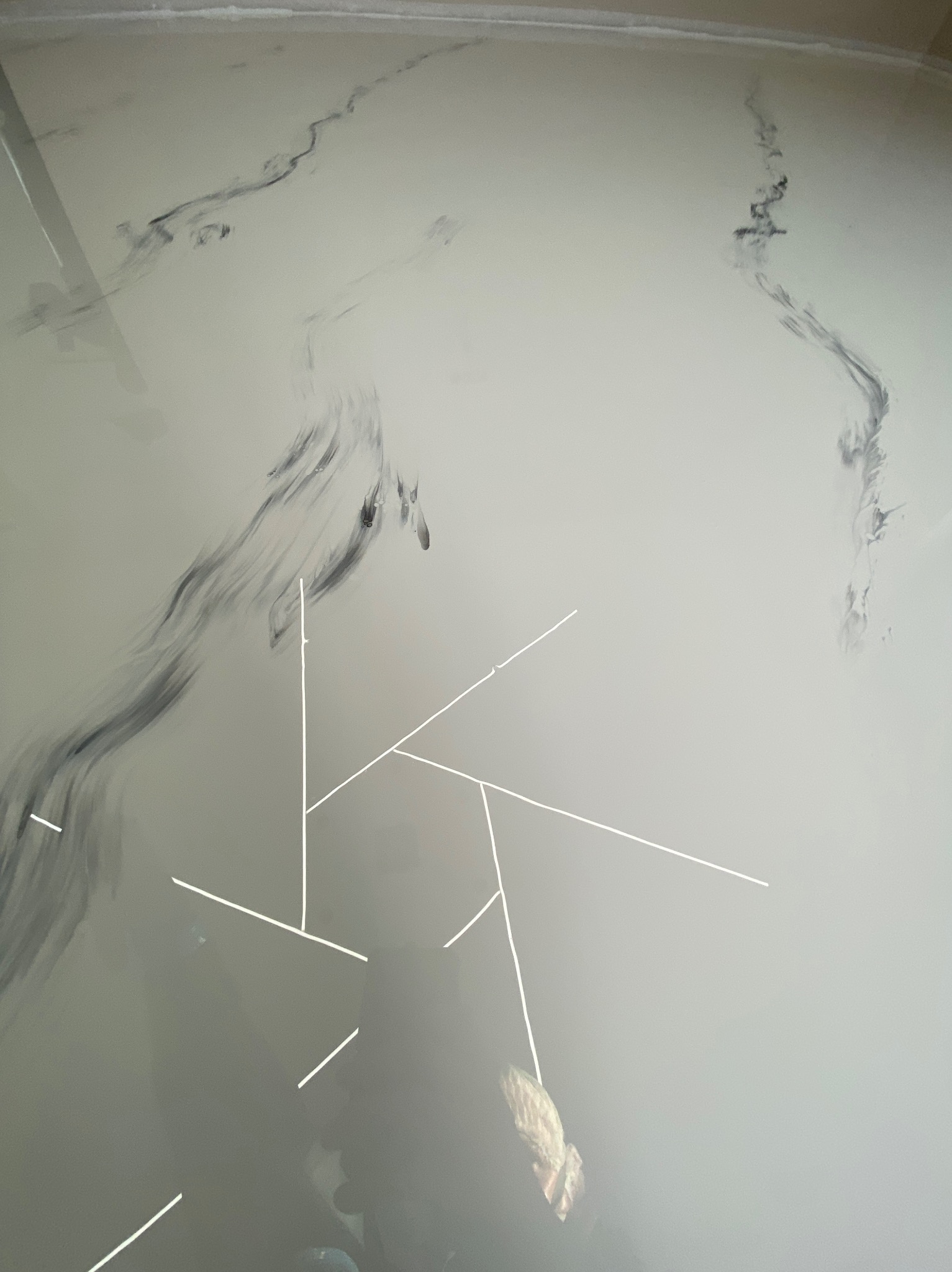 Jasnoszara podłoga z żywicy epoksydowej z czarnymi smugami imitującymi marmur, widoczne białe linie pomocnicze do pomiarów i poziomowania.