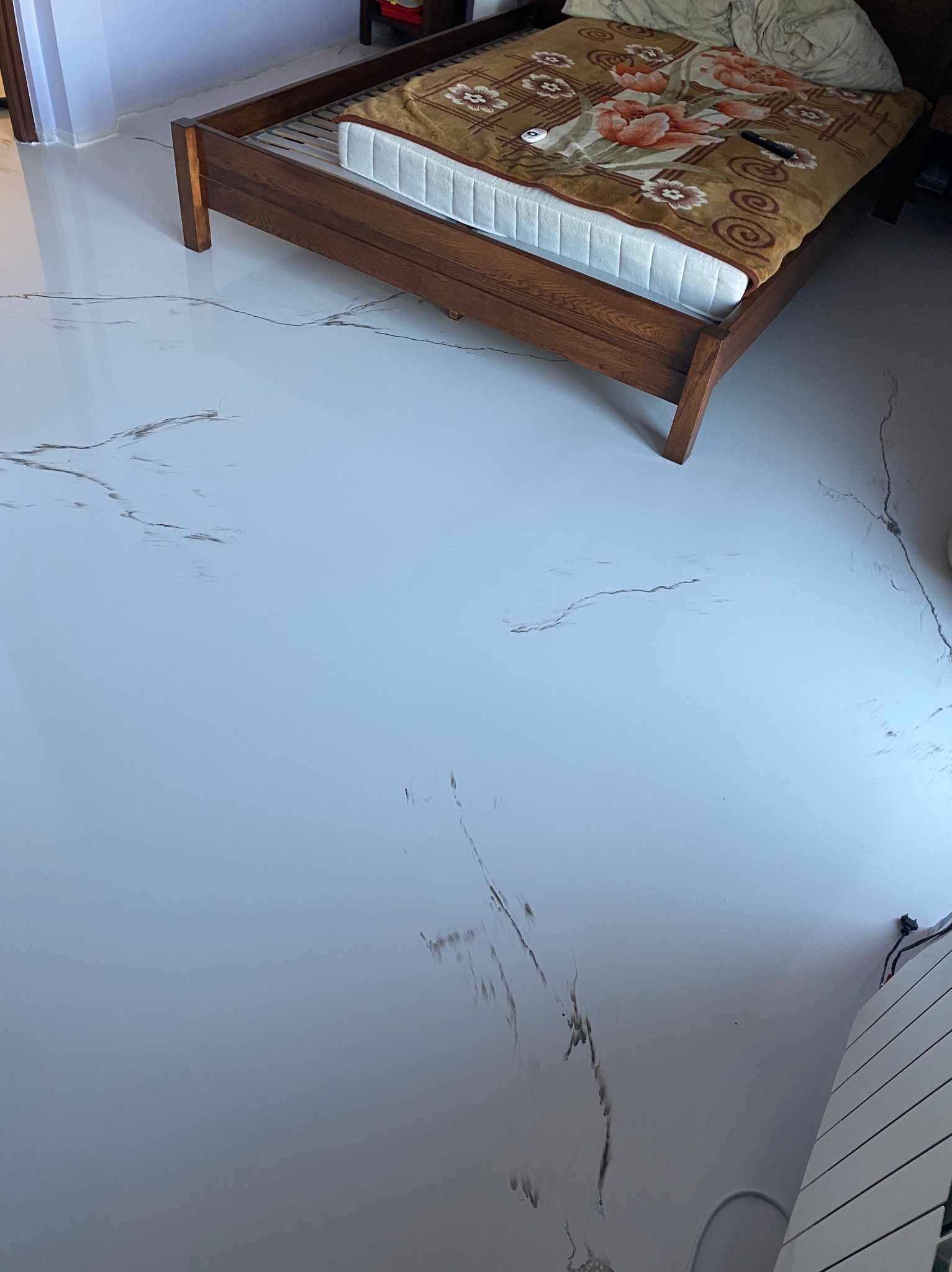 Błyszcząca, biała posadzka z szarymi żyłkami imitującymi marmur w sypialni z drewnianym łóżkiem i grzejnikiem na ścianie.