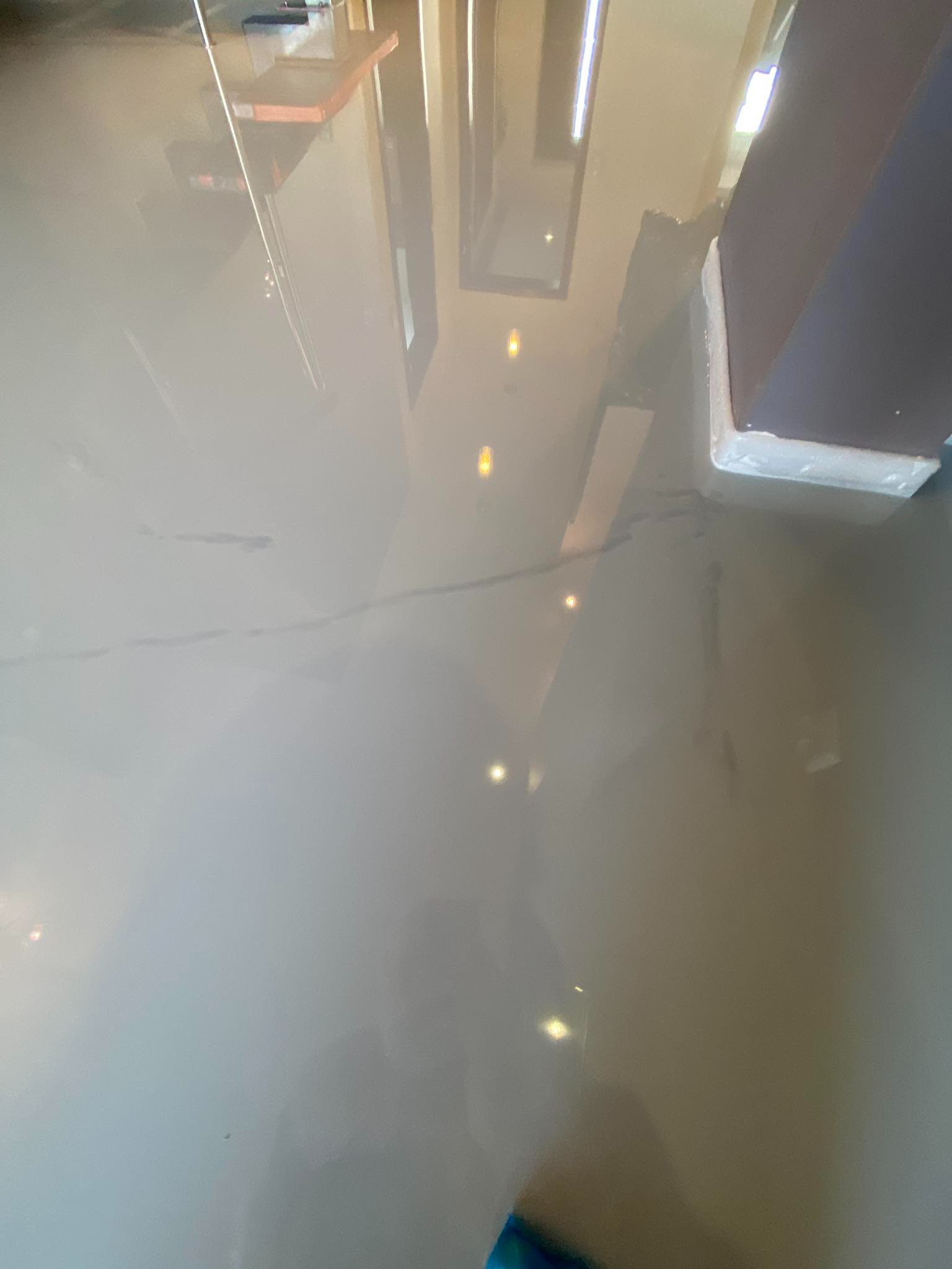 Gładka, błyszcząca posadzka w odcieniach szarości, z widocznym odbiciem sufitu i elementów wyposażenia wnętrza, delikatne smugi i niedoskonałości na powierzchni dodają charakteru.