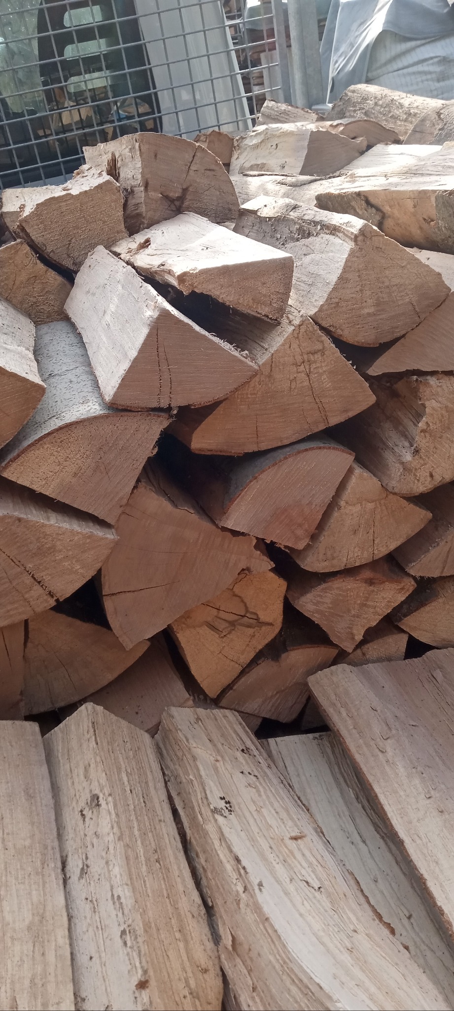 Ułożone kawałki pociętego drewna w koszu z metalowej siatki, widoczne pęknięcia i sęki.