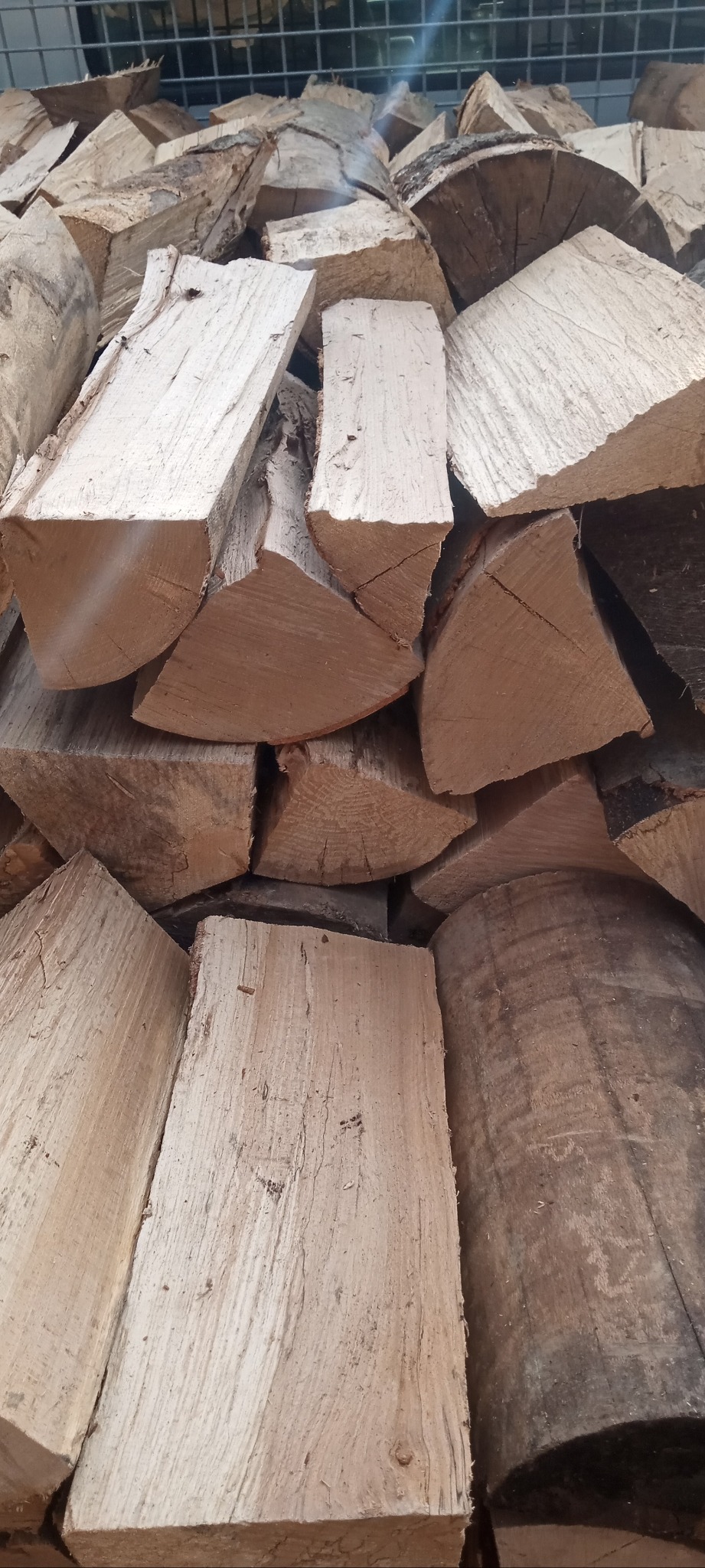 Stos pociętego drewna opałowego ułożonego na metalowej siatce, widoczne słoje i kora.