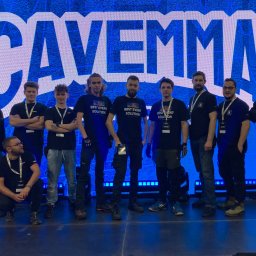 Extreme Sound - Grupa mężczyzn w czarnych koszulkach z napisem 'BEST EVENT SOLUTION' pozuje na tle podświetlonej ściany z dużym logo 'CAVEMMA 2', prawdopodobnie podczas wydarzenia.