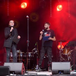 Extreme Sound - Dwoje konferansjerów na scenie oświetlonej czerwonymi światłami, za nimi zestaw perkusyjny i instrumenty muzyczne.