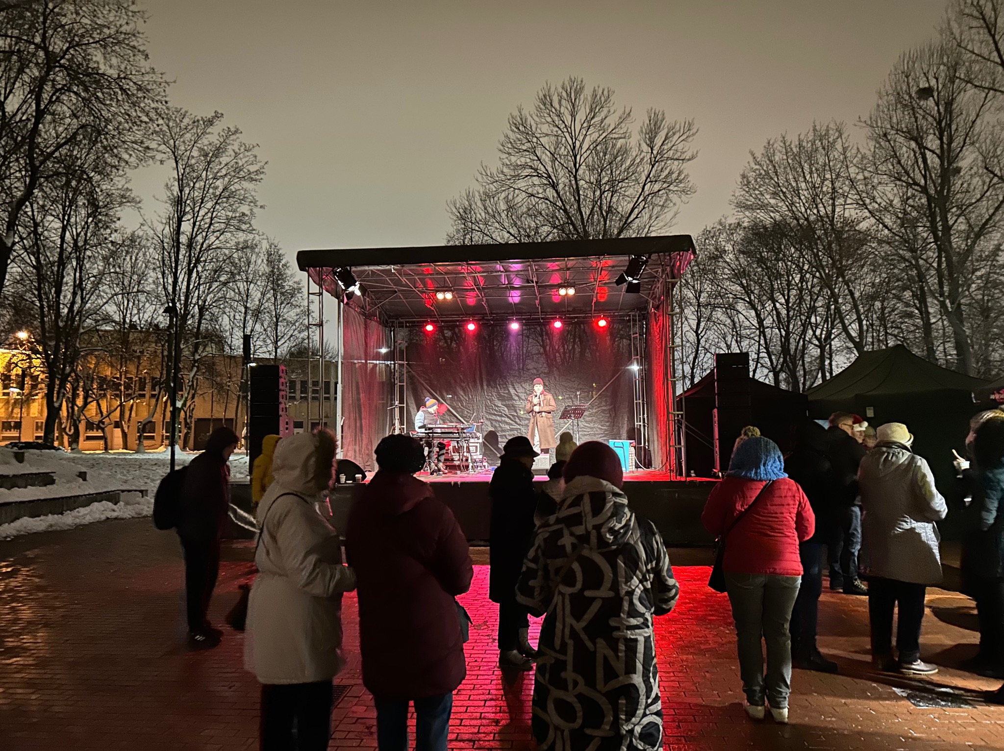 Wieczorny koncert na zewnątrz z publicznością, oświetlona scena z wykonawcami w tle
