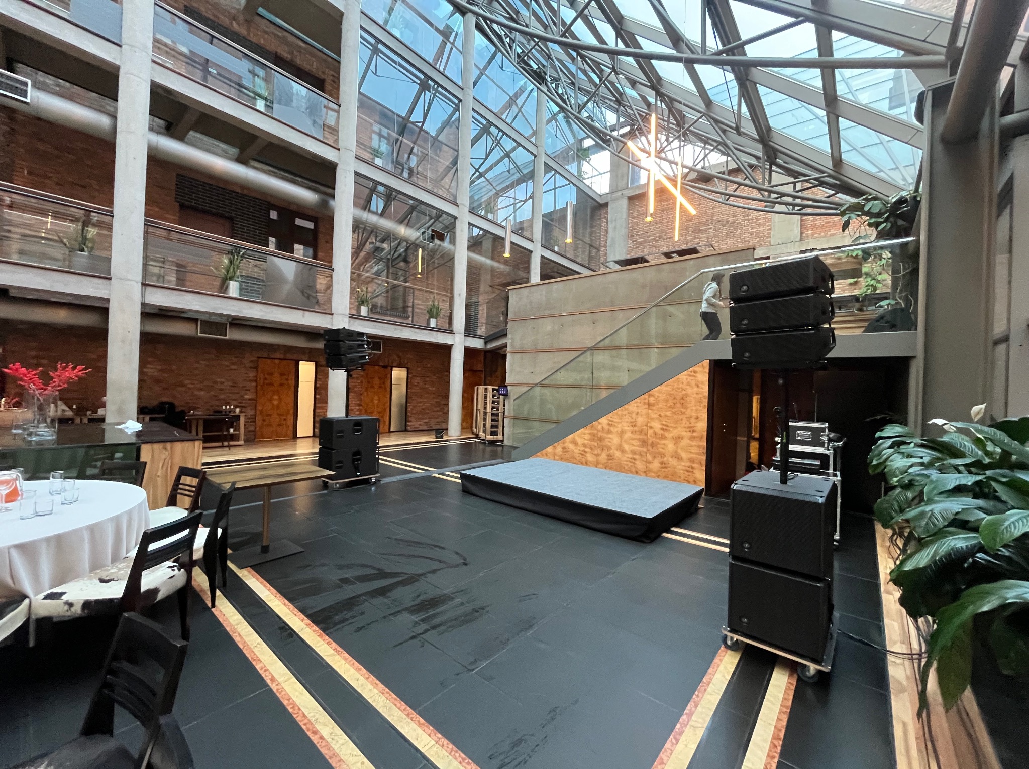 Wnętrze atrium z przygotowanym nagłośnieniem, sceną i stolikami, gotowe na wydarzenie.