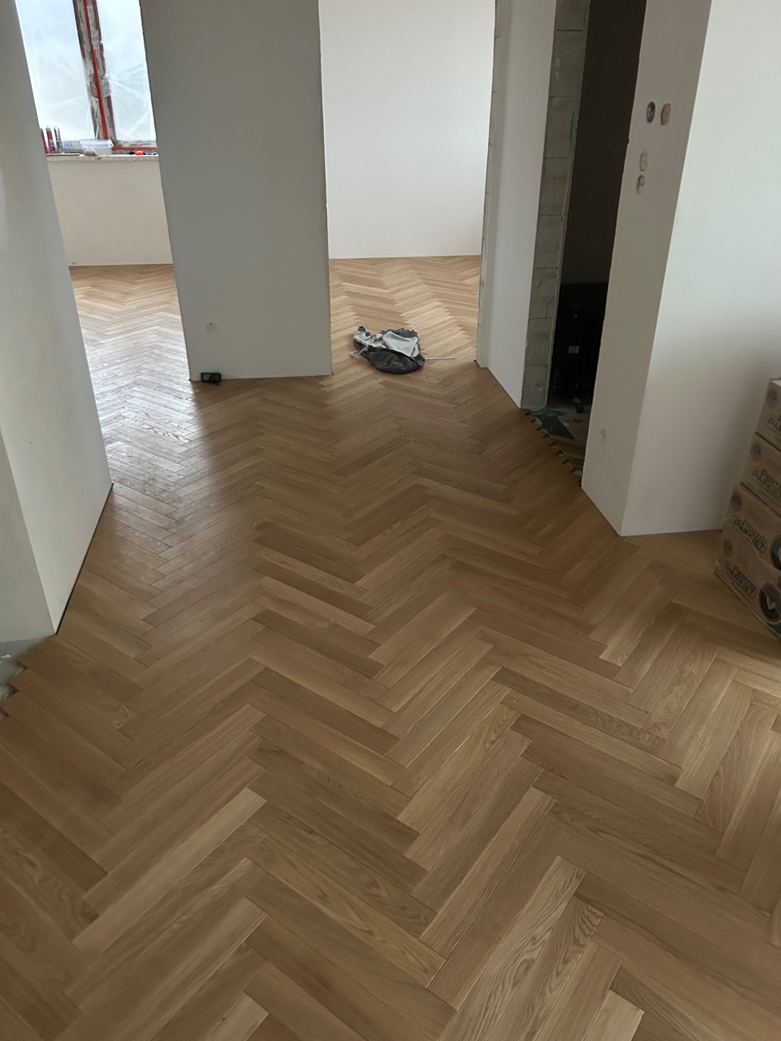 Ułożona podłoga z paneli w jodełkę w nowym mieszkaniu, widoczne kartony z panelami i niedokończone ściany.