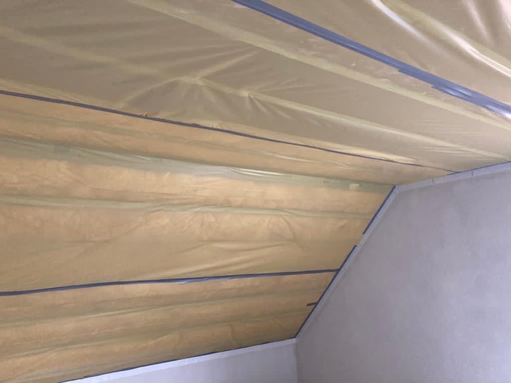 Poddasze zabezpieczone folią i taśmą malarską przed pracami wykończeniowymi, widoczne drewniane belki stropowe.