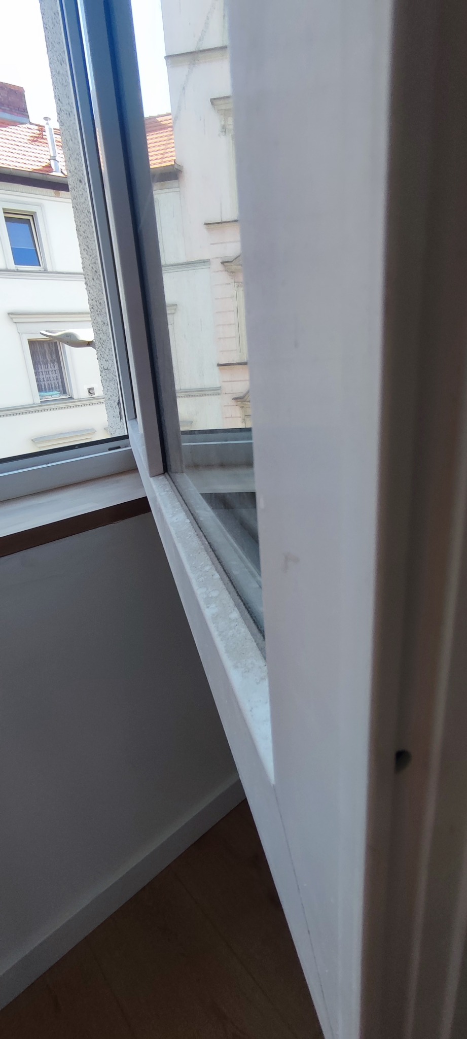 Zabrudzone ramy okienne z widocznym osadem i kurzem, widok na budynki z zewnątrz.