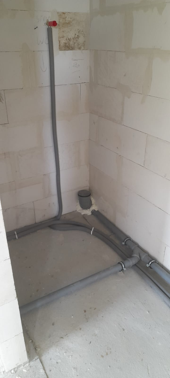 Szare rury instalacji wodnej zamocowane do ściany z betonu komórkowego i podłogi, zabezpieczone pianką montażową w narożniku pomieszczenia.