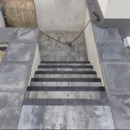 Schody zewnętrzne z kostki brukowej w odcieniach szarości, z widocznymi detalami ułożenia i wykończenia. Kąt ujęcia z góry podkreśla geometrię stopni.