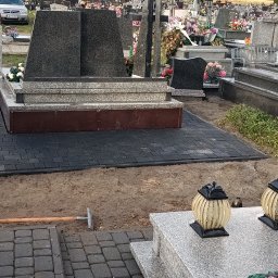 MR KOP - Ciemnoszara kostka brukowa ułożona wokół nagrobka na cmentarzu. Widoczne narzędzia ogrodnicze i lampiony. Ujęcie z poziomu gruntu, w tle inne nagrobki.