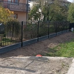 MR KOP - Czarny, metalowy płot z podmurówką z szarego betonu, skrzynka na listy z numerem 24. Częściowo rozpakowane narzędzia monterskie obok słupka. Widok na ulicę i dom.