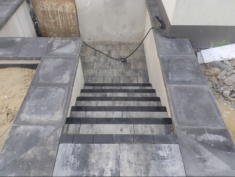 Schody zewnętrzne z kostki brukowej w odcieniach szarości, z widocznymi detalami ułożenia i wykończenia. Kąt ujęcia z góry podkreśla geometrię stopni.