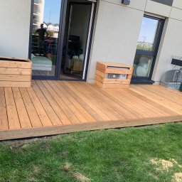 Vasyl Yatsko - Nowoczesny taras z jasnego drewna z drewnianymi donicami i obudową klimatyzatora, widok na trawnik i budynek mieszkalny.