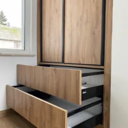 Szafa przesuwna z drewnopodobnymi frontami, czarnymi obramowaniami i dwoma otwartymi szufladami z systemem Blum.