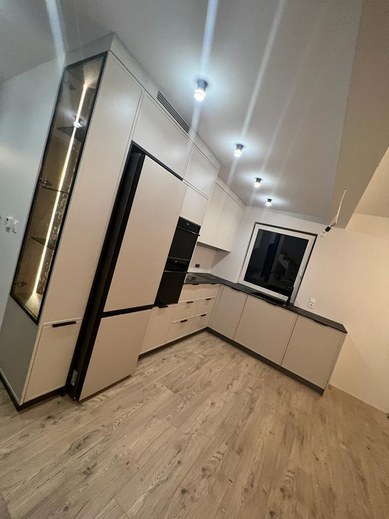 Nowoczesna kuchnia z beżowymi szafkami, czarnymi akcentami i oświetleniem LED w witrynie, widziana z perspektywy podłogi z paneli.