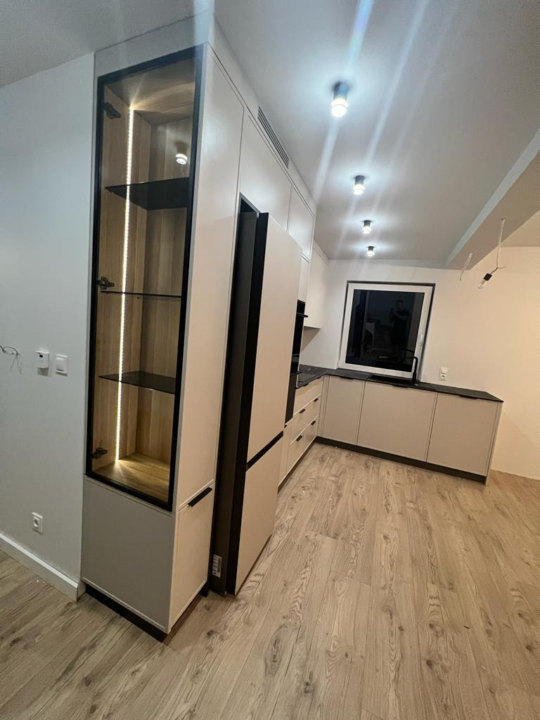 Nowoczesna kuchnia z zabudową meblową w odcieniach beżu i szarości, z wysoką witryną podświetloną LED, widok z perspektywy podłogi.