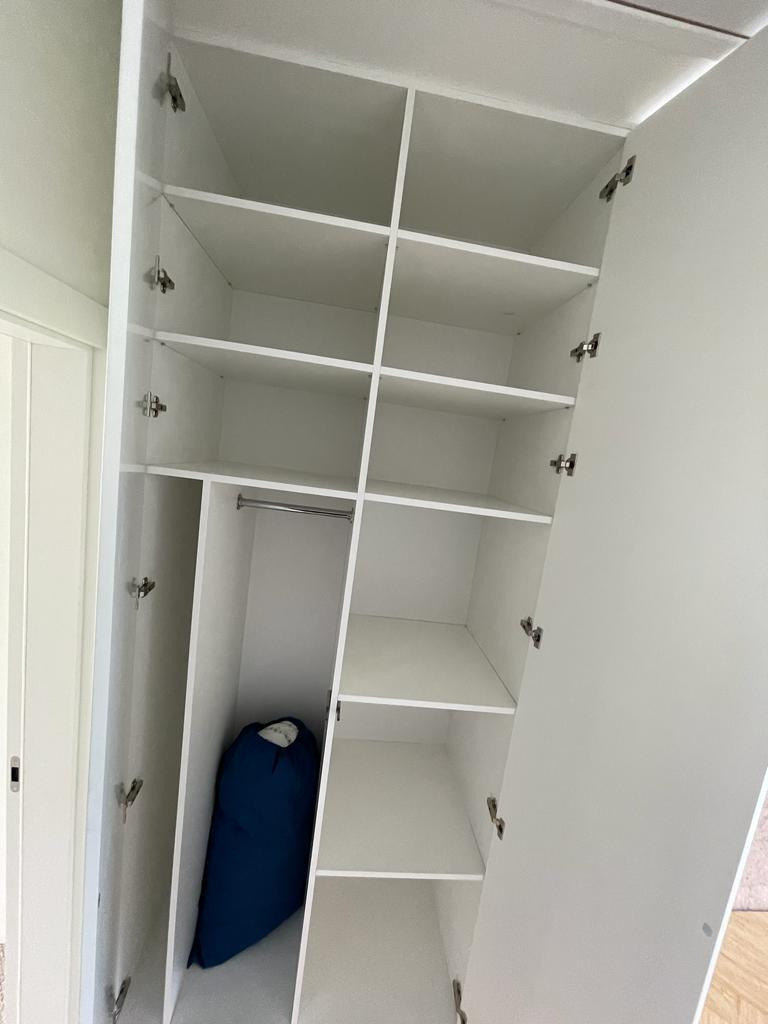 Wnętrze białej, otwartej szafy z półkami, w dolnej części widoczny zwinięty śpiwór w kolorze granatowym.