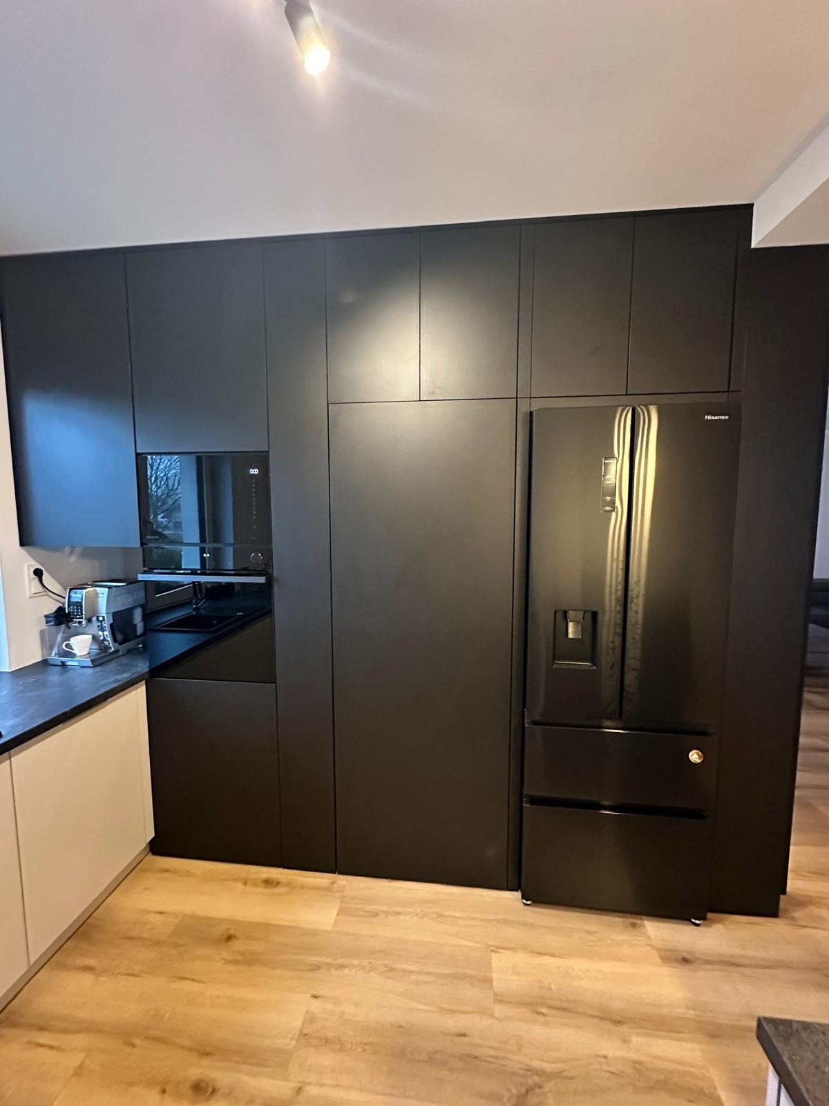 Nowoczesna kuchnia z zabudową w kolorze grafitowym, obejmująca lodówkę Hisense, piekarnik i szafki, z blatem w odcieniach szarości i drewnianą podłogą.