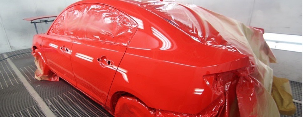 Czerwony samochód w trakcie lakierowania w Dębicy, zabezpieczony folią i papierem, widoczna metalowa podłoga lakierni.