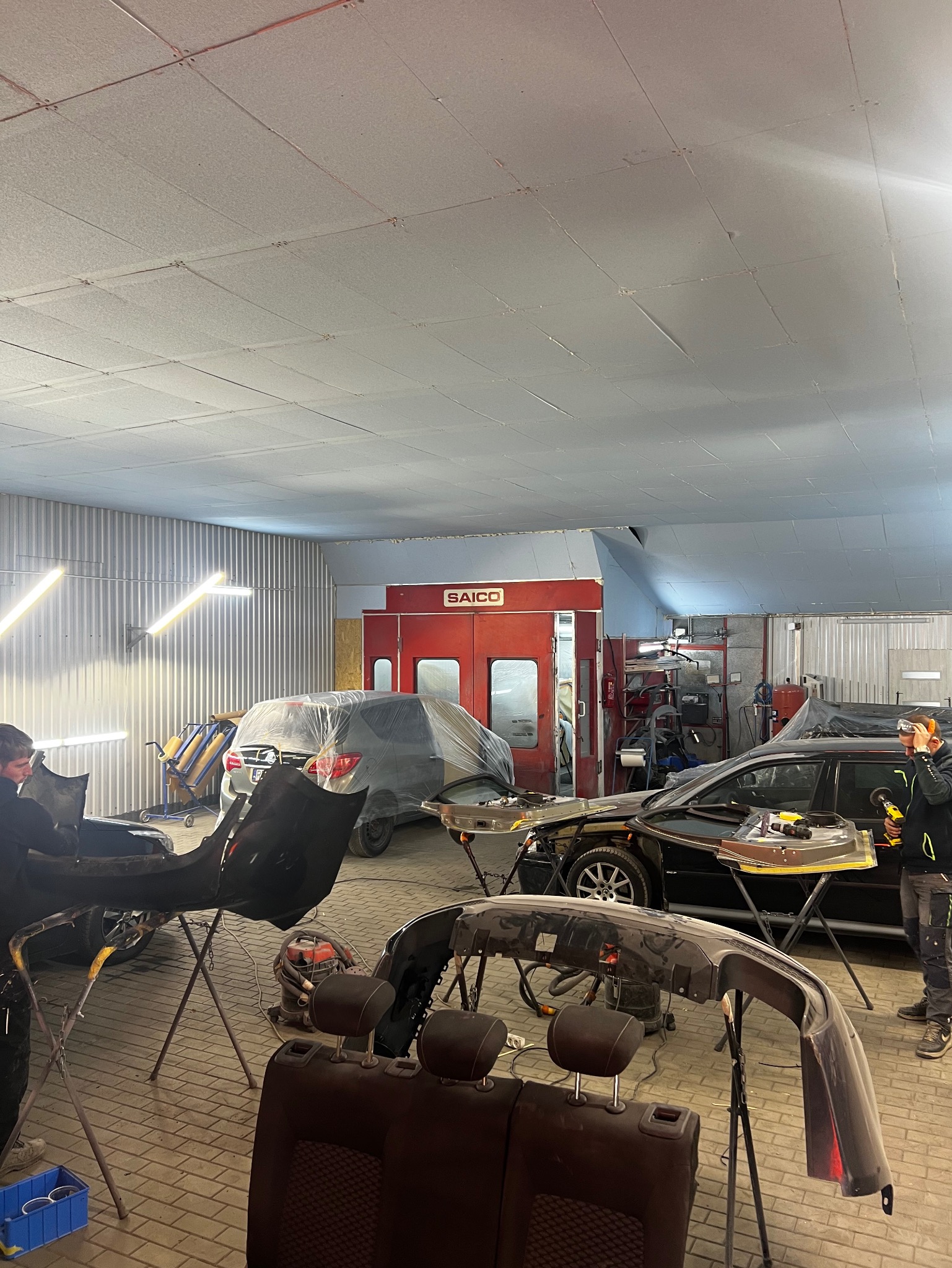 Warsztat w Dębicy: przygotowanie elementów karoserii i zderzaków do lakierowania; widoczna komora lakiernicza SAICO w tle.