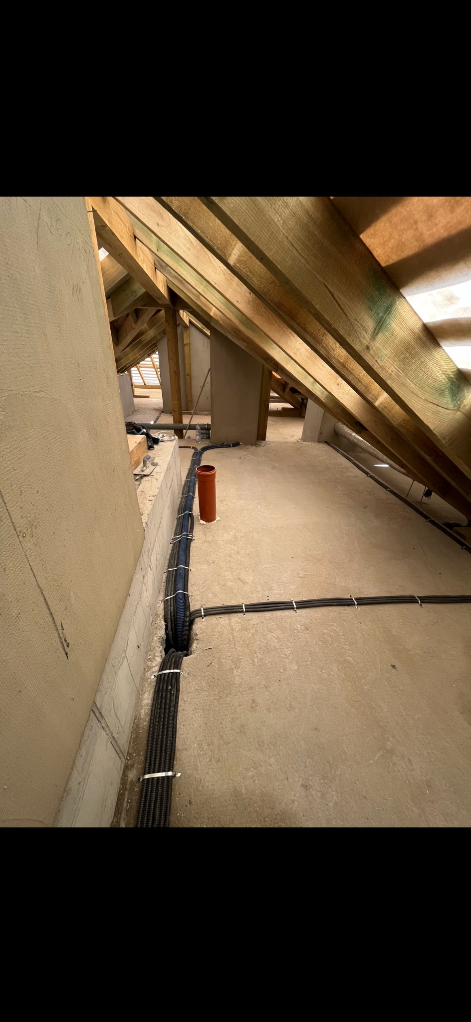 Wiązka kabli elektrycznych prowadzona wzdłuż ściany na poddaszu, zabezpieczona opaskami zaciskowymi, z widoczną konstrukcją drewnianą dachu i fragmentem instalacji wentylacyjnej.