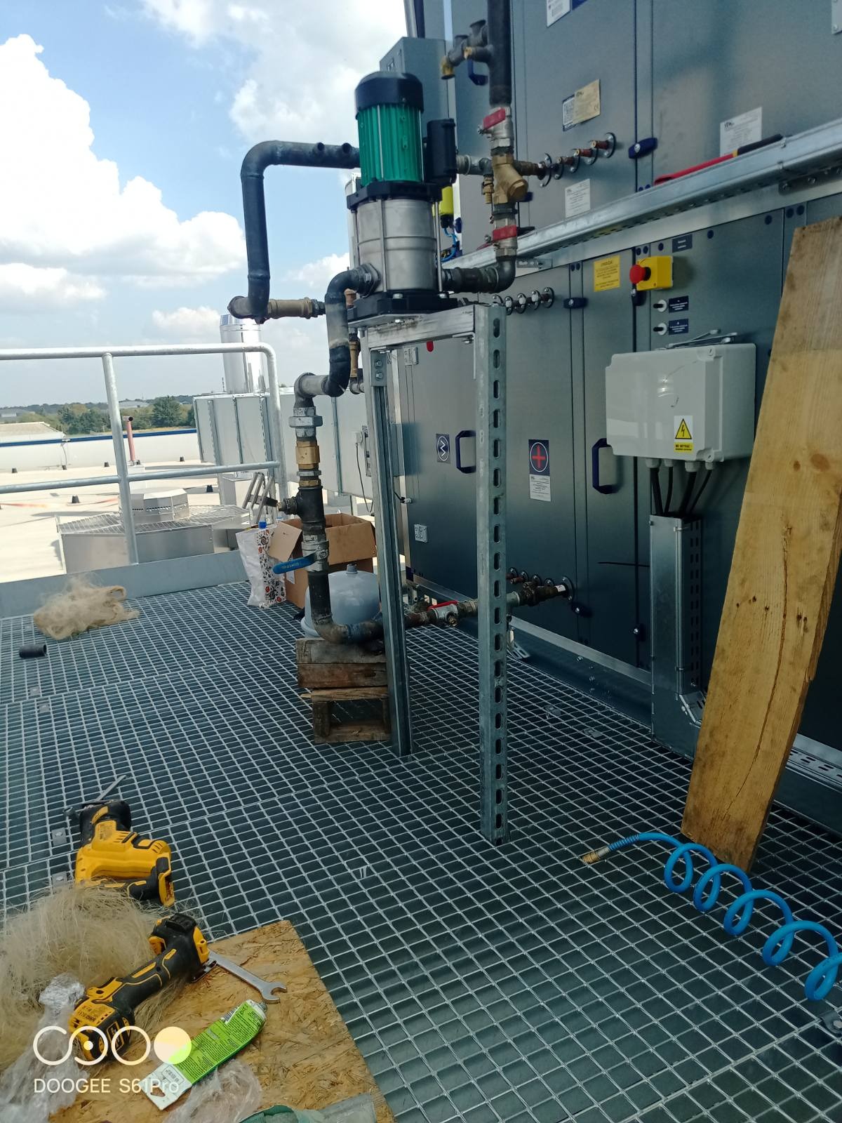 Instalacja przemysłowa z rurami i pompą na dachu w Łowinek. Widoczne narzędzia i elementy montażowe. Metalowa konstrukcja i kratownica podłogowa.