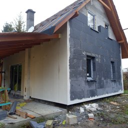 Fasad Servis - Dom jednorodzinny w trakcie prac elewacyjnych: część ściany ocieplona grafitowym styropianem, druga część z surowym tynkiem, widoczne rusztowanie, dach z częściowo położoną papą.