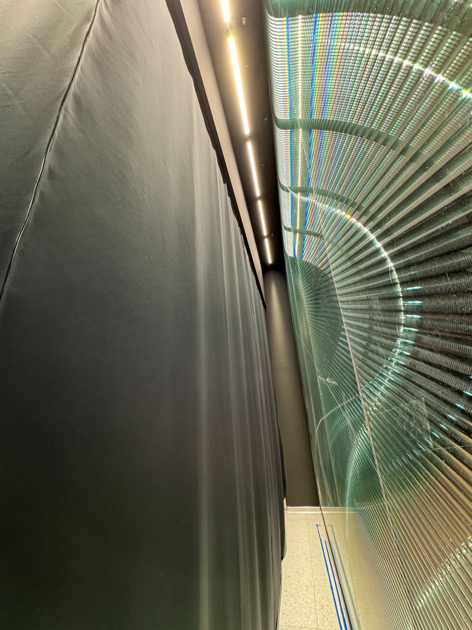 Ciemna, trudnopalna zasłona zaciemniająca z widocznym szwem obok dekoracyjnej, podświetlonej ściany z żaluzji w budynku.