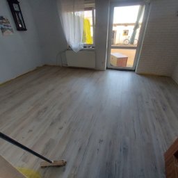 RAFI - BUD RAFAŁ ROMANOWSKI - Pokój po położeniu jasnych paneli podłogowych z widoczną fakturą drewna, listwy przypodłogowe jeszcze nie zamontowane, widoczna szczotka do zamiatania.