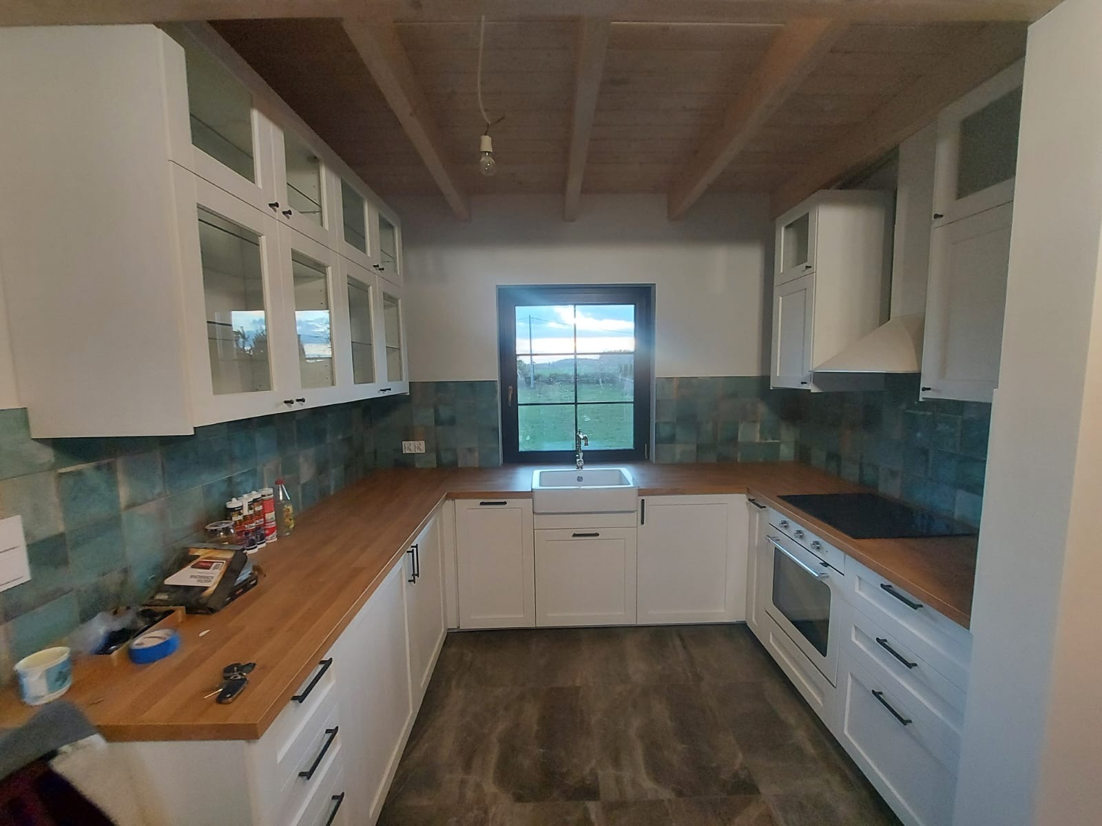 Jasna kuchnia z drewnianym blatem w Skórczu, zielone płytki na ścianie, widok z okna na zewnątrz.