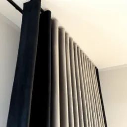 Draperie zaciemniające w odcieniach szarości i czerni, zawieszone na podwójnym karniszu sufitowym, układające się w regularne fałdy.