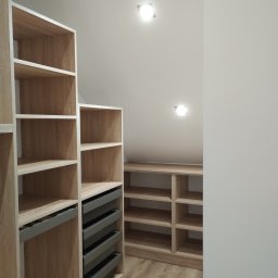 Robert Dzierzgwa R.D.R. - Jasna garderoba z półkami i szufladami w zabudowie pod skośnym sufitem, oświetlona punktowymi lampami.