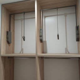 Robert Dzierzgwa R.D.R. - Wnętrze szafy wnękowej z jasnego drewna z drążkami na ubrania i pantografami.