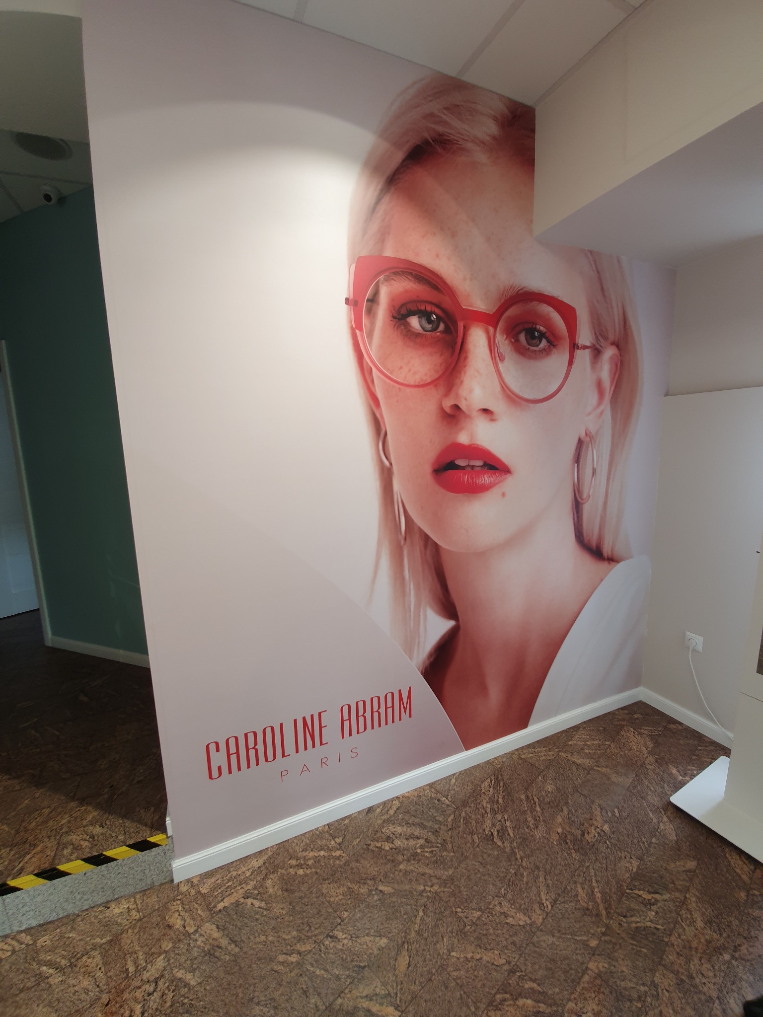 Wnętrze z naklejoną na ścianie grafiką przedstawiającą portret kobiety w okularach marki Caroline Abram Paris.